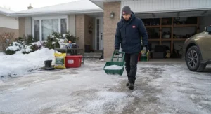 Homeowner applying ice melter from a garage safety kit to a frosty Canadian driveway.